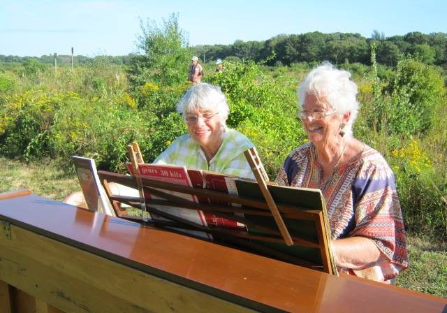 Two older people playing piano outdoors
