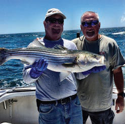 Two men aft on a charter boat holding a large striped bass