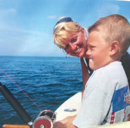 Boy with fishing rod concentrating on pulling in a fish with mom smiling beside him