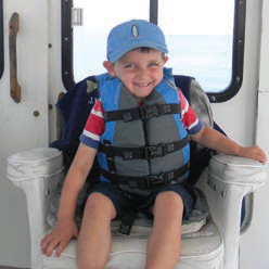 Little boy with lifejacket and big grin sitting in the cabin of a charter fishing boat