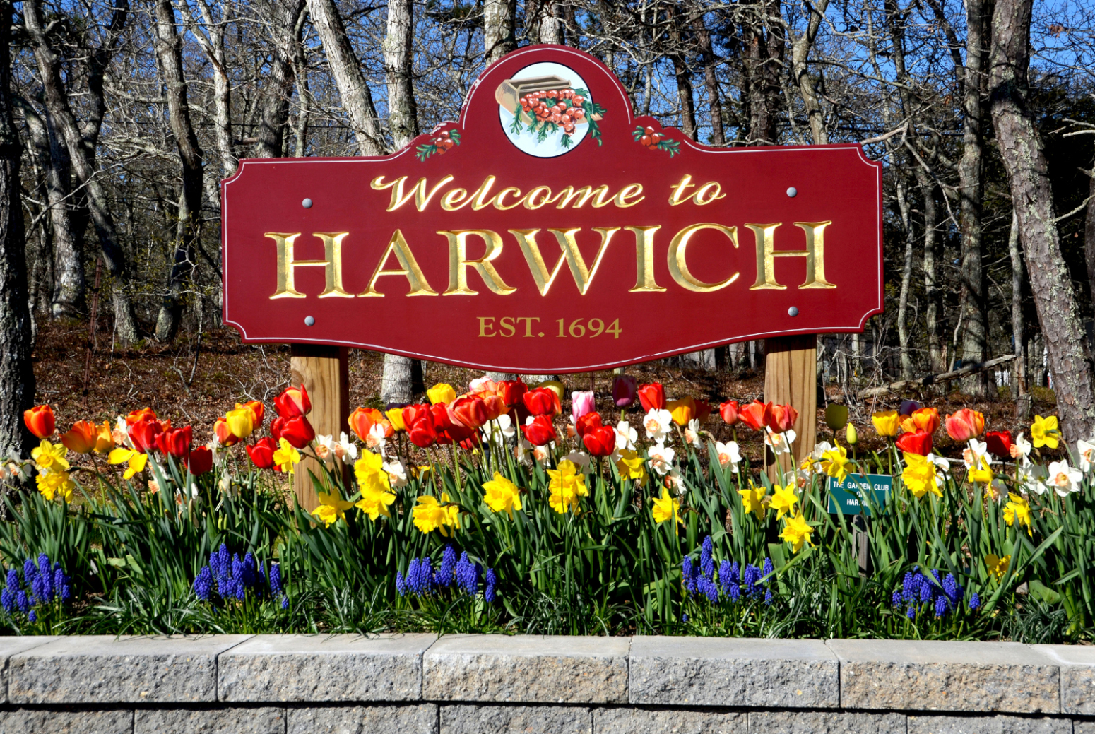 Welcome to Harwich sign with spring flowers in front and woods behind