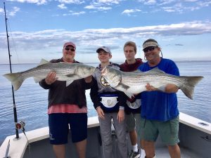 Four men on deck of charter fishing boat with two enormous striped bass