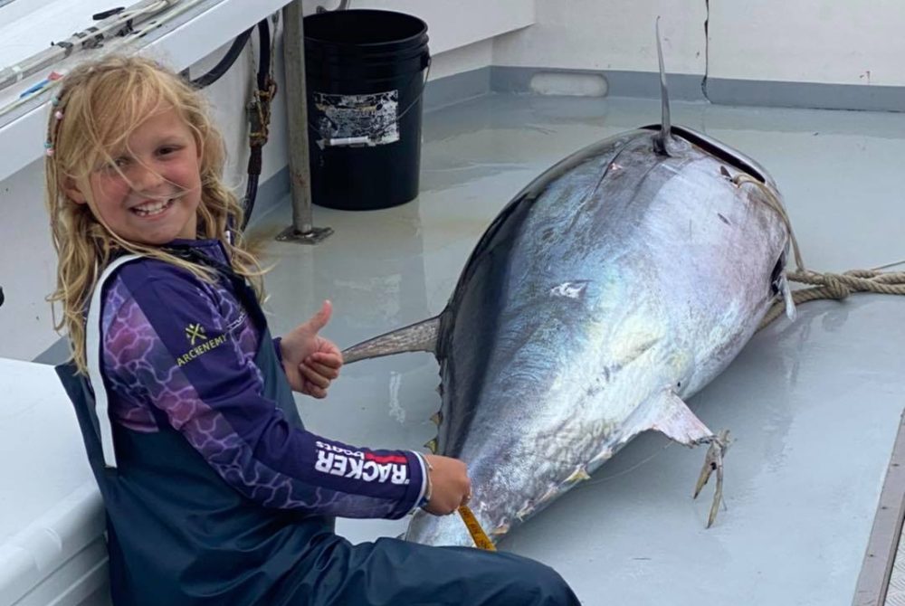 Young fisherman girl with bluefin tuna on deck of boat