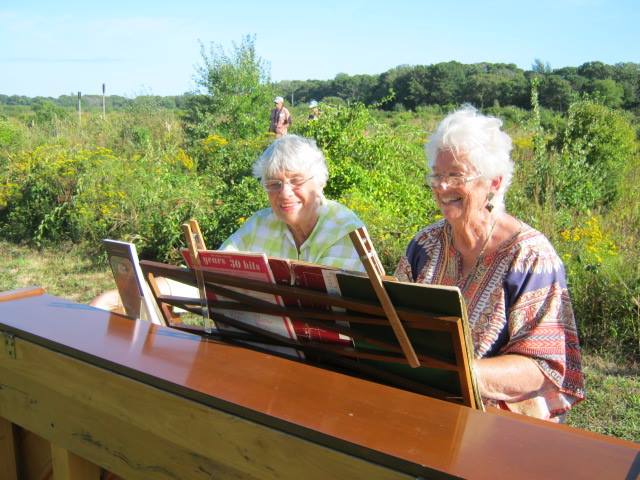 Two smiling women playing piano outdoors